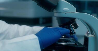 Man in a lab coat uses a microscope sitting at a desk in a medical laboratory. Close-up of his face photo