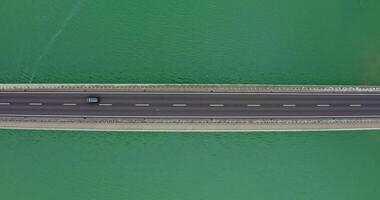 Narrow road bridge with cars passing over it, over a river with a shallow ripple of waves. recording from a drone photo