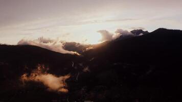 The light of rising sun breaks through fluffy white clouds over the peaks of the Alps. Village in a lowland between mountains at dusk, drone , Austria photo