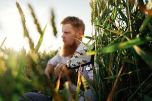 Country, musician is with guitar on the ground. Man in white shirt is on the agricultural field photo