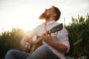 Concentrated ,,on, playing the guitar. Man in white shirt is on the agricultural field photo