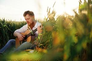 Concentrated on playing the guitar. Man,, in ,white shirt is on the agricultural field photo