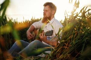 Country musician is with guitar ,,on ,the ,ground. Man in white shirt is on the agricultural field photo