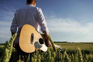 Musician, is with acoustic guitar. Man in white shirt is on the agricultural field photo