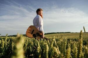 Guitar in, hands. Man in white shirt is, on the agricultural field photo