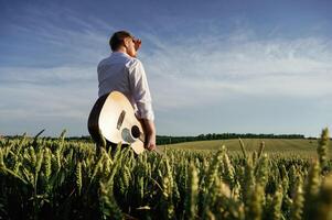 Musician is with acoustic guitar.. Man in white shirt is on the agricultural field photo