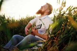 Concentrated ,on ,playing the guitar. Man in white shirt is on the agricultural field photo