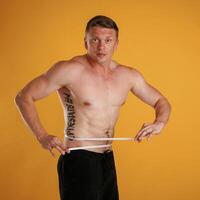 Measuring ,the waist, muscular ,,guy. Man is against background in the studio photo