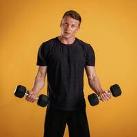 Sportsman is with dumbbells, standing again,,st background in the studio photo