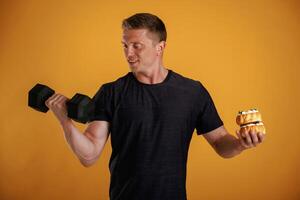 Dumbbell or cake, choice. Man ,is,, against background in the studio photo
