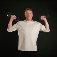 Powerful sportsman, is holding dumbbells. Against background in the studio photo