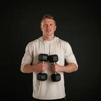 Powerful sportsman, is, holding dumbbells. Against background in the studio photo