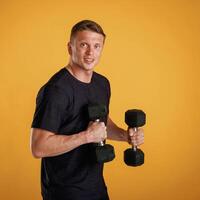 Sportsman is ,,with dumbbells,, standing against background in the studio photo