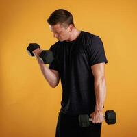 Sportsman is with dumbbells, standing, against background in the studio photo