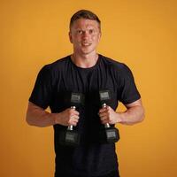 Sportsman is ,with ,dumbbells, standing against background in the studio photo