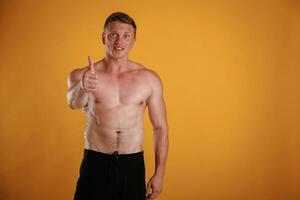 Without shirt, showing thumb up, smiling. Man is against background in the studio photo