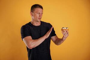 Say no ,to, sugar, holding cake, don't like it. Man is against background in the studio photo