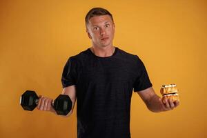 Dumbbell, or, cake, choice. Man is against background in the studio photo