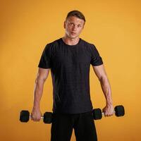 Sportsman ,is with dumbbells, standing against background in the studio photo