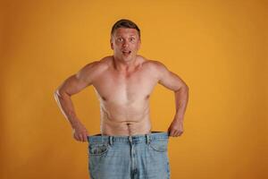 Weight, loss, shocked by results, big and huge pants or jeans. Man is against background in the studio photo