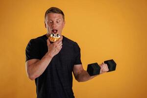 Dumbbell ,or cake, choice. Man is against background in the studio photo