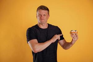 Say, no to sugar, holding cake, don't like it. Man is against background in the studio photo