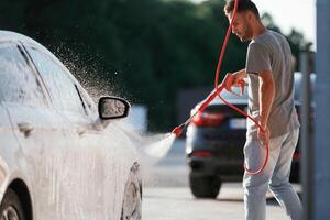 Water high pressure stream, car wash. Man is with his automobile outdoors photo