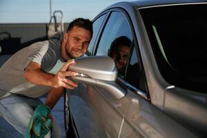 Looking at the ,side mirror, cleared. Man is with his car outdoors photo