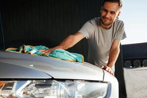Guy is polishing ,the surface of automobile by using cloth. Man is with his car outdoors photo
