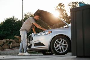Beautiful, sunlight. Hood is opened, guy is repairing the automobile. Man is with his car outdoors photo