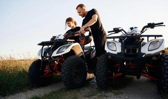 Showing, how, the machine works. Father and daughter are with ATV outdoors photo