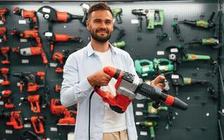 Plural,, perforator in hands. Man is in the, hardware shop photo