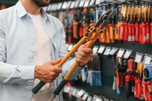 Orange, colored wire cutter, holding in hands. Man is in the hardware shop photo