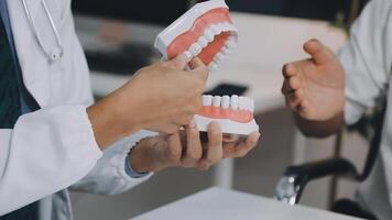 A dentist is holding a tooth model in front of a patient video
