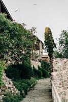 Ancient Balkan walkway framed by stone ruins and lush green trees on a warm summer day with rustic charm and peaceful vibe of village life echoing through history and architectural textures photo