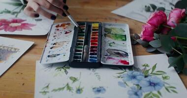 Woman artist mixes watercolor paints with a brush to get the right color. Close-up of female hands with a paintbrush photo