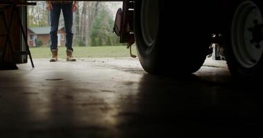 Man walks into an indoor garage approaching a tractor, male legs in stylish brown boots close-up photo