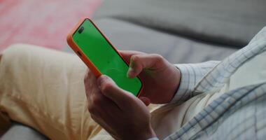 Phone with a green screen in men's hands. The man scrolls the pages with his finger. Close-up of men's hands photo