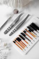 Eyelash Extension Tools Flat Lay A minimalist composition featuring pink and clear mascara wands arranged on a light surface, accompanied by delicate white flowers, creating a soft and elegant photo