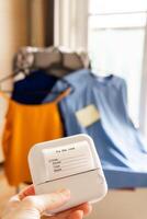 mano participación mini térmico impresora con ropa desordenar Lista de Verificación en brillante minimalista habitación con organizado vestidos en perchas en antecedentes concepto de inteligente hogar guardarropa planificación y clasificación foto
