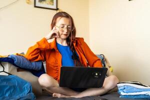 Woman working remotely from bed surrounded by neatly folded clothes highlighting the blend of digital nomadism, remote productivity and conscious wardrobe management in sustainable lifestyle photo
