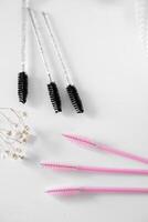 Flat Lay of Beauty Tools and Mascara Wands A minimalist composition featuring pink and clear mascara wands arranged on a light surface, accompanied by delicate white flowers, creating a soft and photo