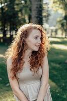 Woman with curly red hair standing silently in forest sunlight shining through trees rainbow glare on body green nature warm tones soft expression peaceful energy captured in authentic atmosphere photo