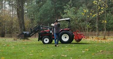 Young man climbs out of an agricultural vehicle tired after working in the field, taking off his baseball cap and wiping his forehead with his hand, on a sunny autumn day photo