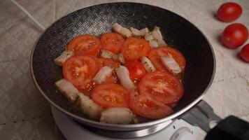 Sizzling sounds fill the air as fresh tomatoes and bacon cook together in a frying pan, showcasing cooking techniques in a cozy home kitchen at night. video