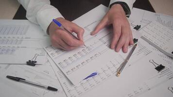 A highly professional workspace featuring hands actively writing on various financial documents and analysis sheets video