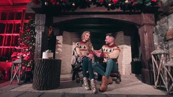 Couple in love spend time together at home. Young man and beautiful girl in knitted Christmas sweaters sitting at fireplace. Christmas background. video