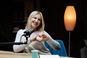 Smiling woman making heart shape with hands during podcast recording. photo