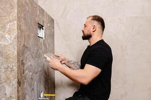 Tiler installing large format tile on bathroom wall. photo