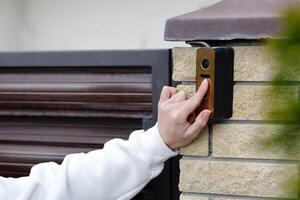 Woman pressing button on modern intercom system at building entrance photo